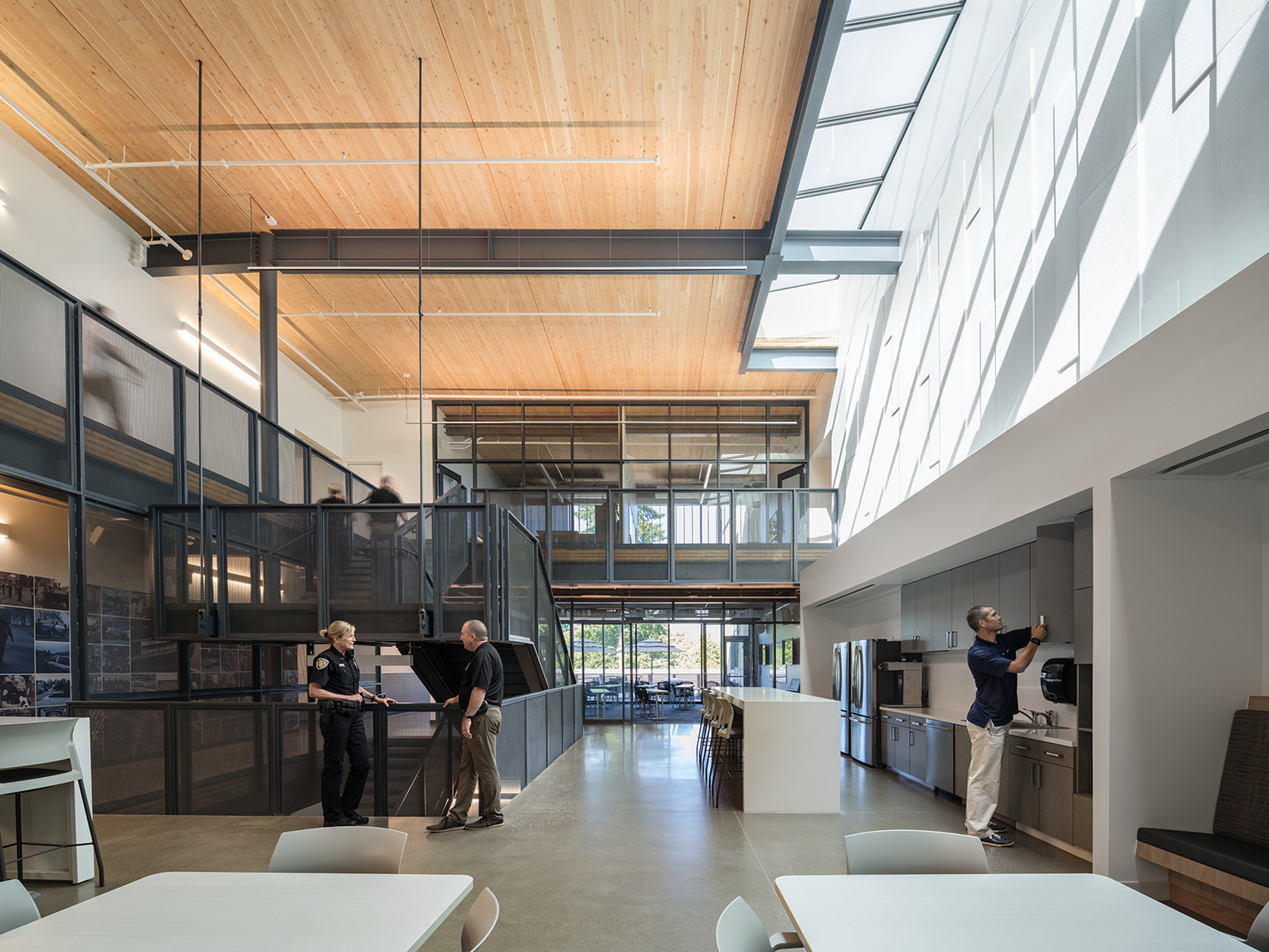 Large double-height Beaverton Public Safety Center break room featuring polished concrete floors, a mass timber ceiling, large skylights and a metal staircase with open hallway above.