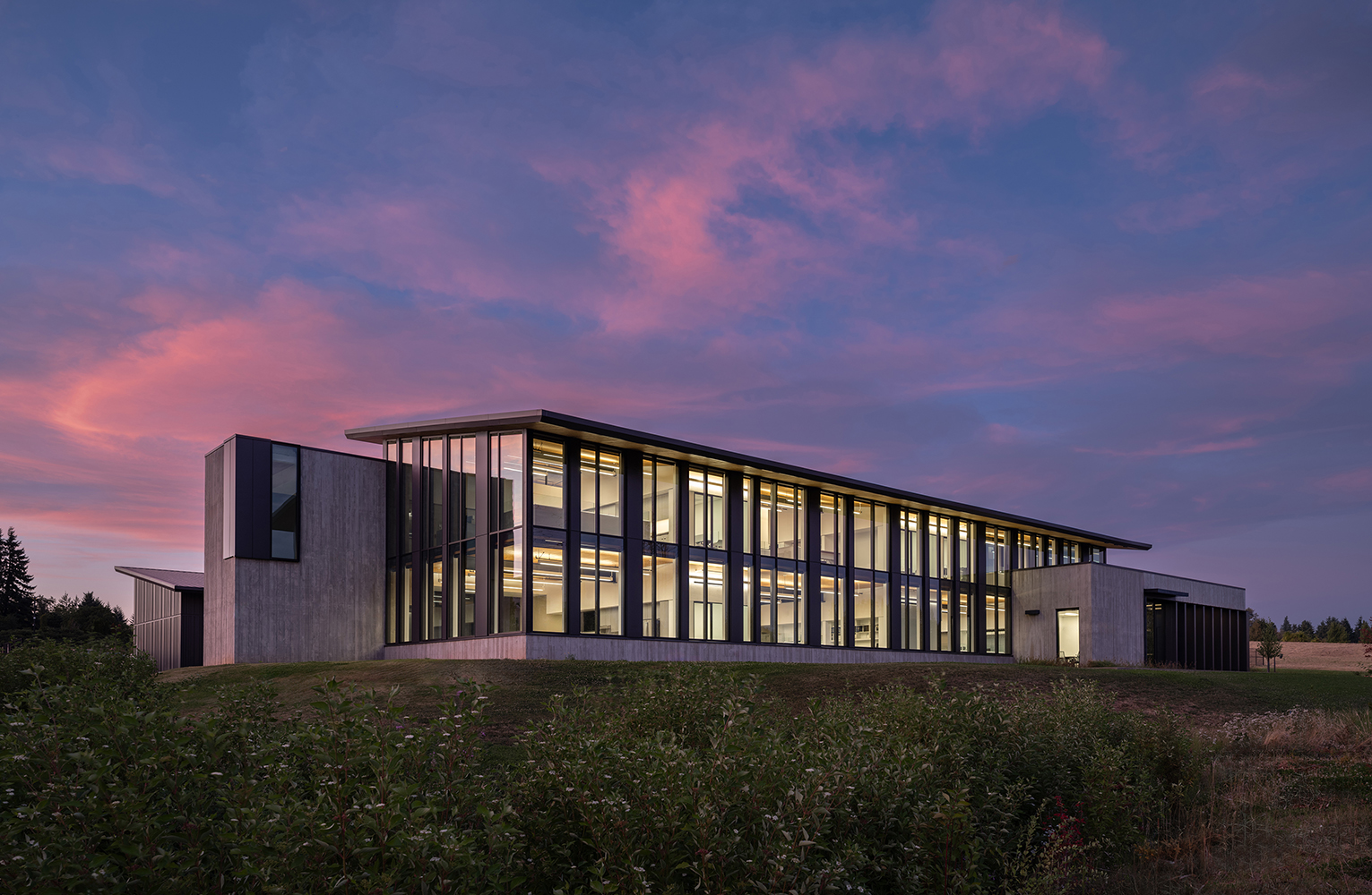The Sunrise Water Authority administrative building glows at dusk, with its tall glazed façade and concrete forms set against a vibrant pink and blue sky.