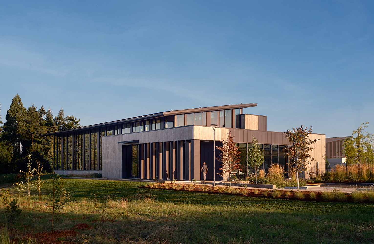 Morning light illuminates the Sunrise Water Authority administrative building, where tall vertical fins, generous glazing, and new landscaping frame the southeast entrance as a staff member walks inside.