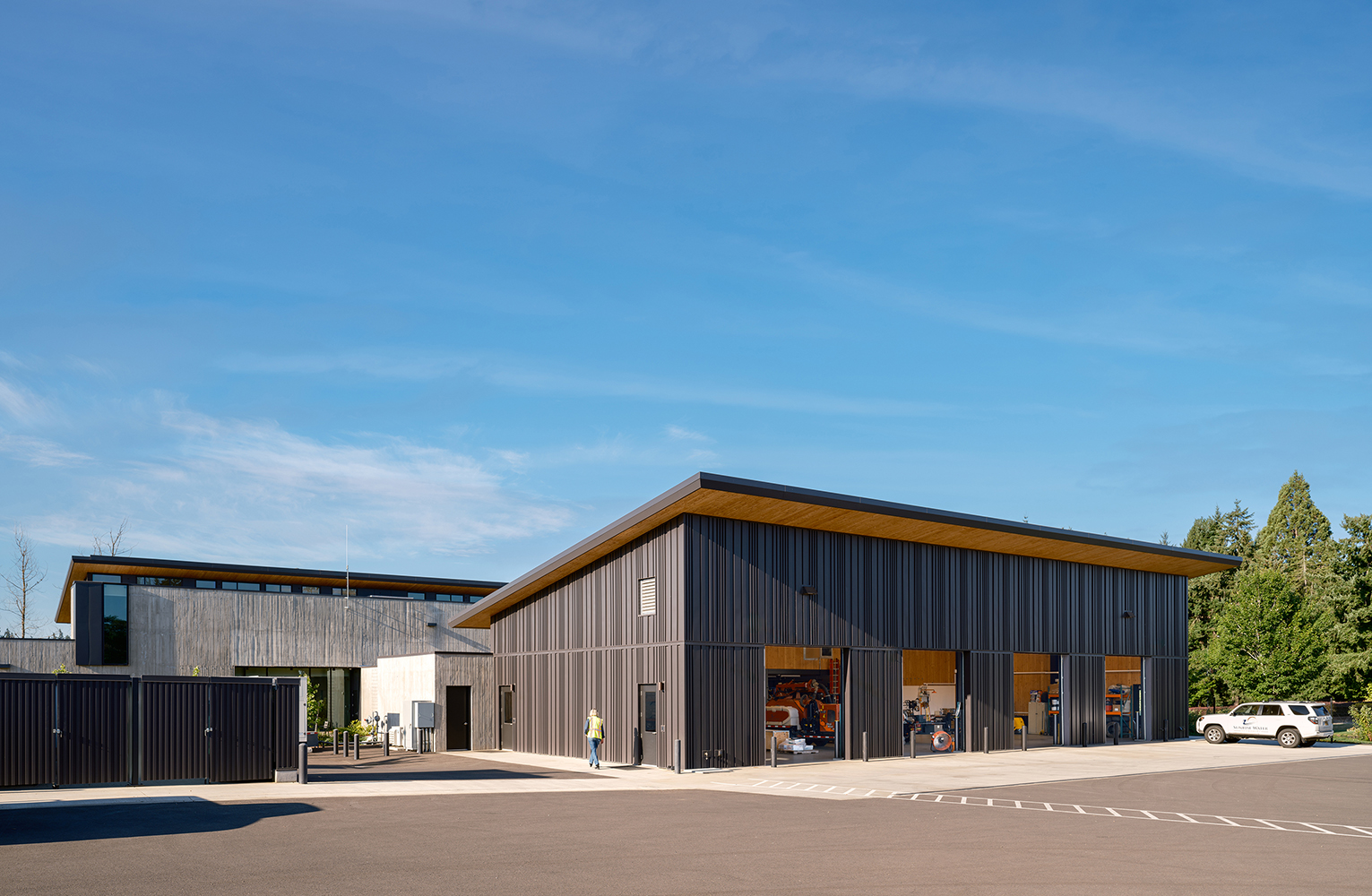 The Sunrise Water Authority field operations shop opens to the yard, with equipment visible through tall bay doors and staff moving between the shop and adjacent site.