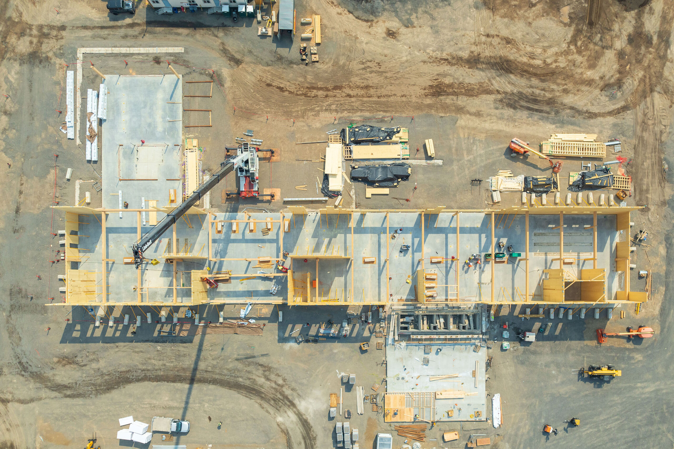 Aerial view of a large construction site with a long, L-shaped building taking shape