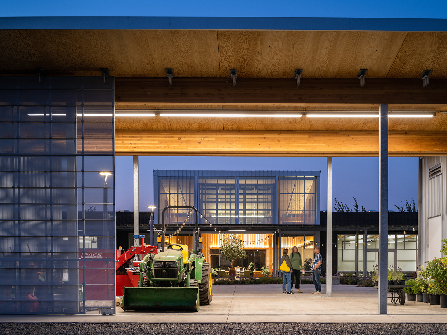 Looking through a gardening equipment building at dusk to see glowing classroom building in background