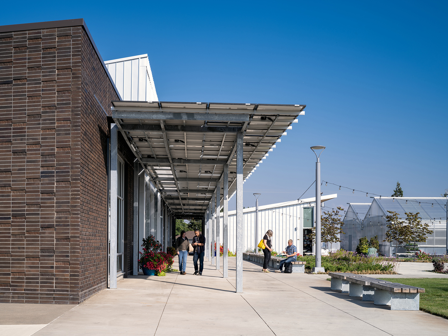 Two people walking next to a building, under a solar canopy