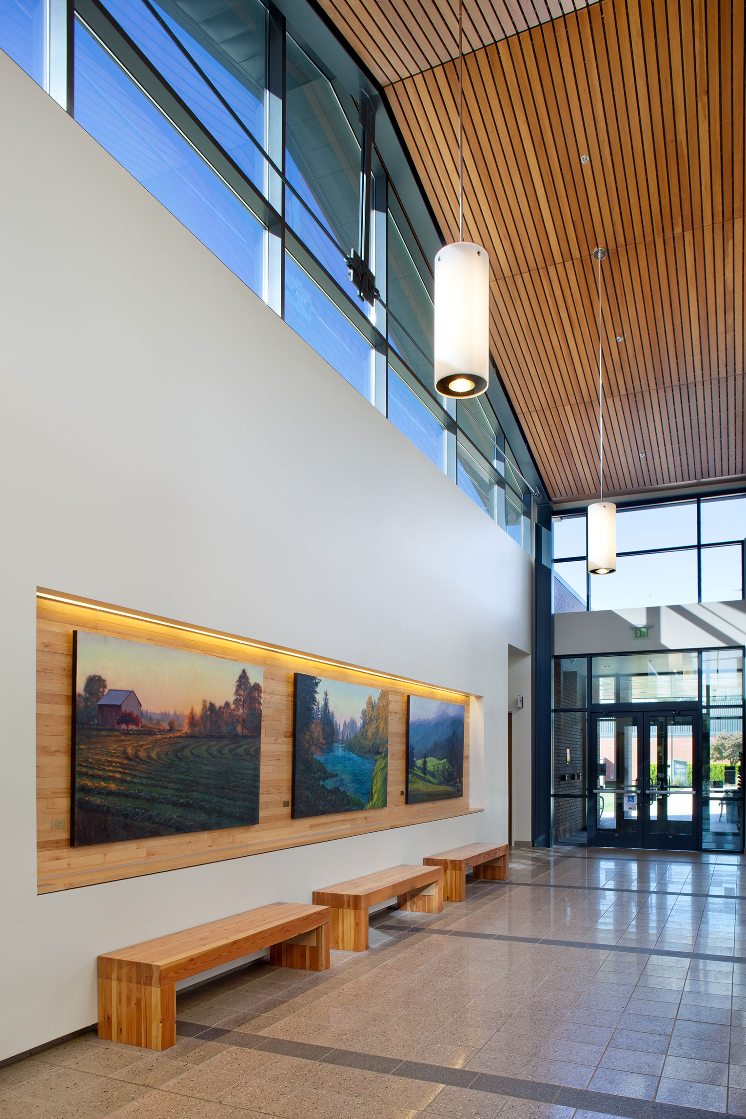 Lobby of a library with clerestory above and three paintings hung side by side on the wall