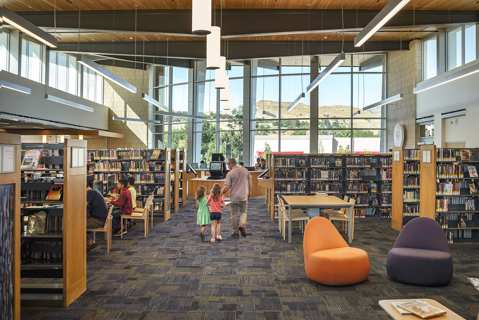 Father walking daughters through library reading room with views to the foothills in the distance