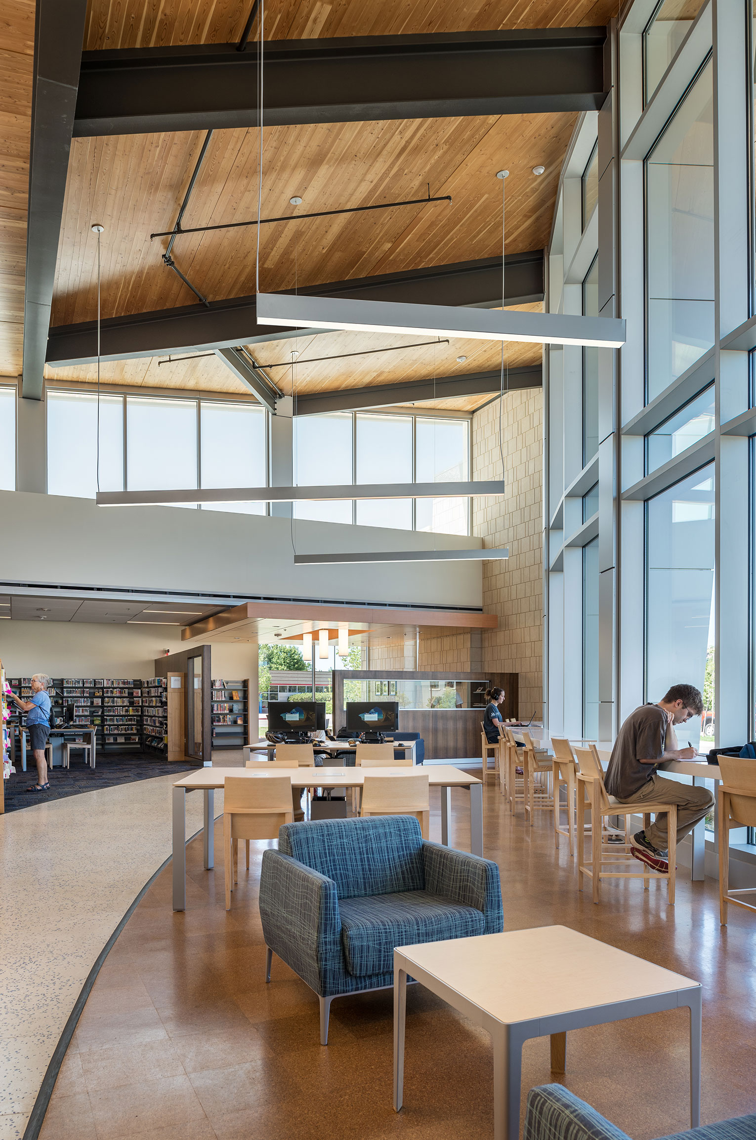 Man sitting at counter next to floor-to=ceiling windows, studying in the library