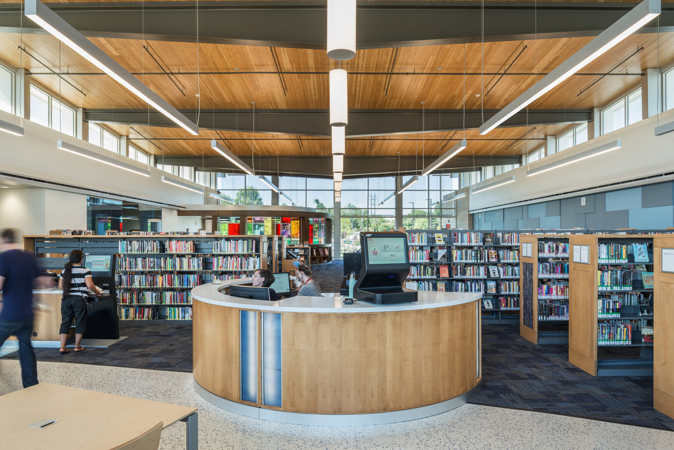 Interior view of a library with the circulation desk in the foreground and book shelves in the background.