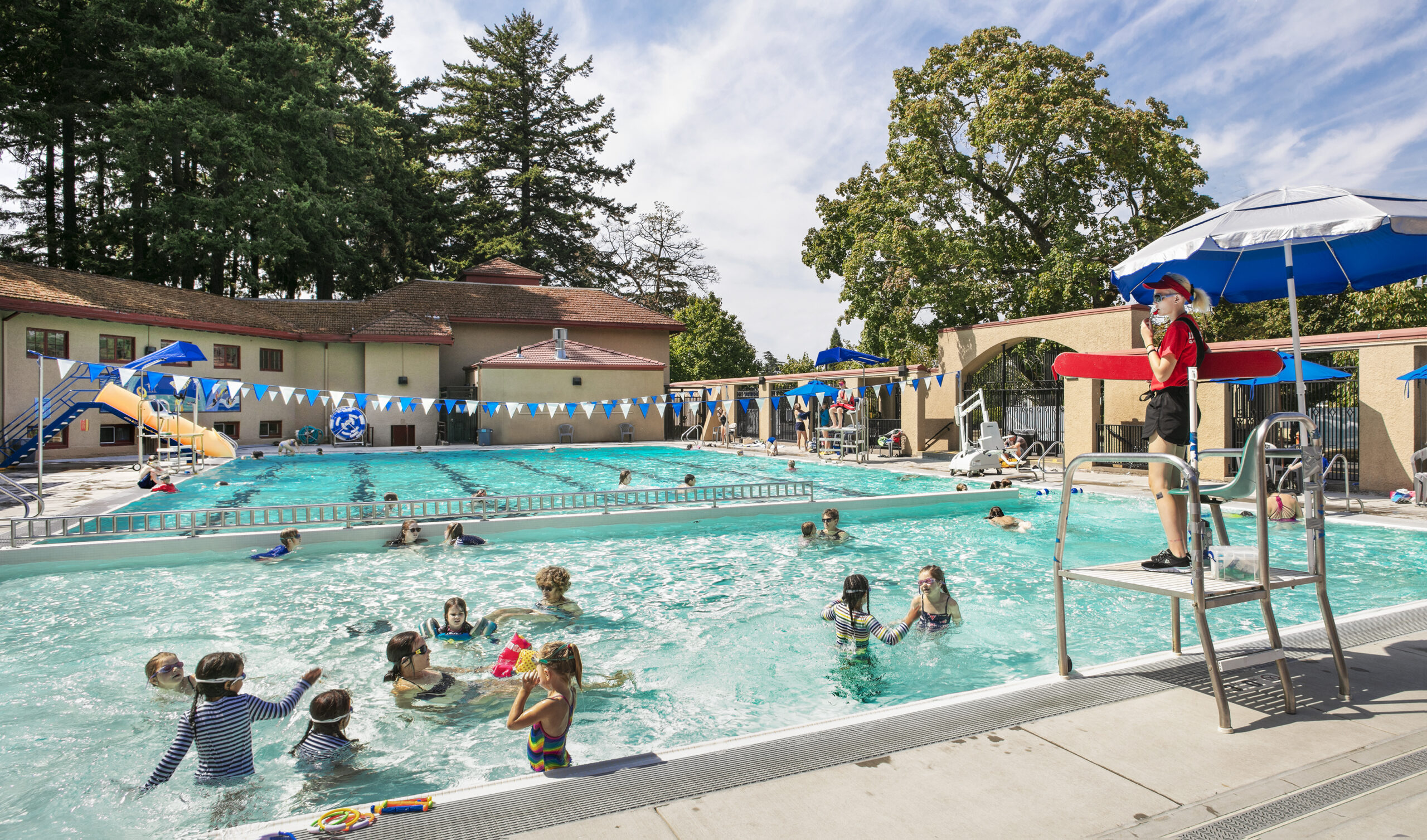 Swimming pool on a summers da, full of children with a lifeguard looking on