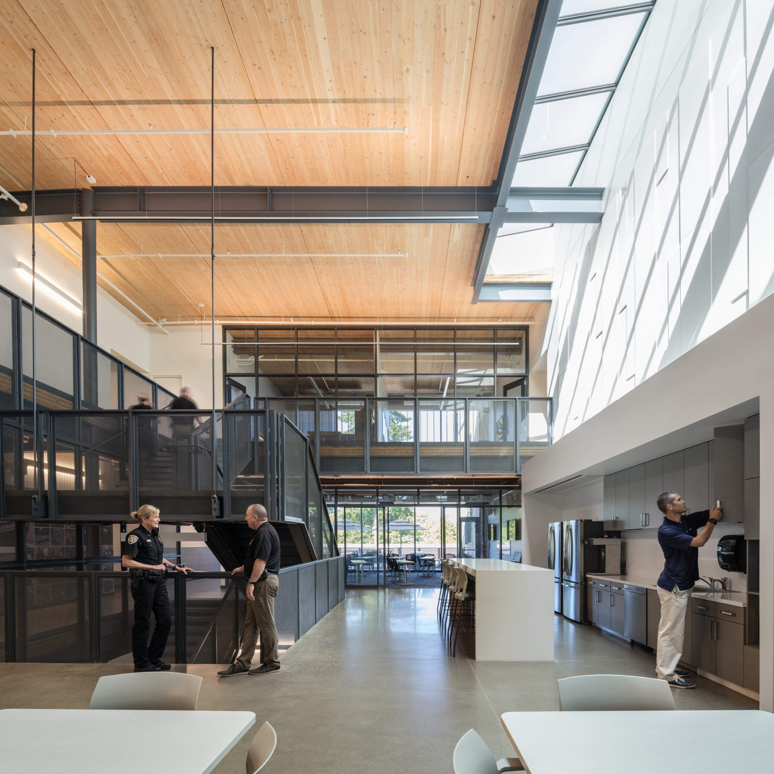 Male and female police officers casually chatting in a large, double-height break room with mass timber ceiling and skylights