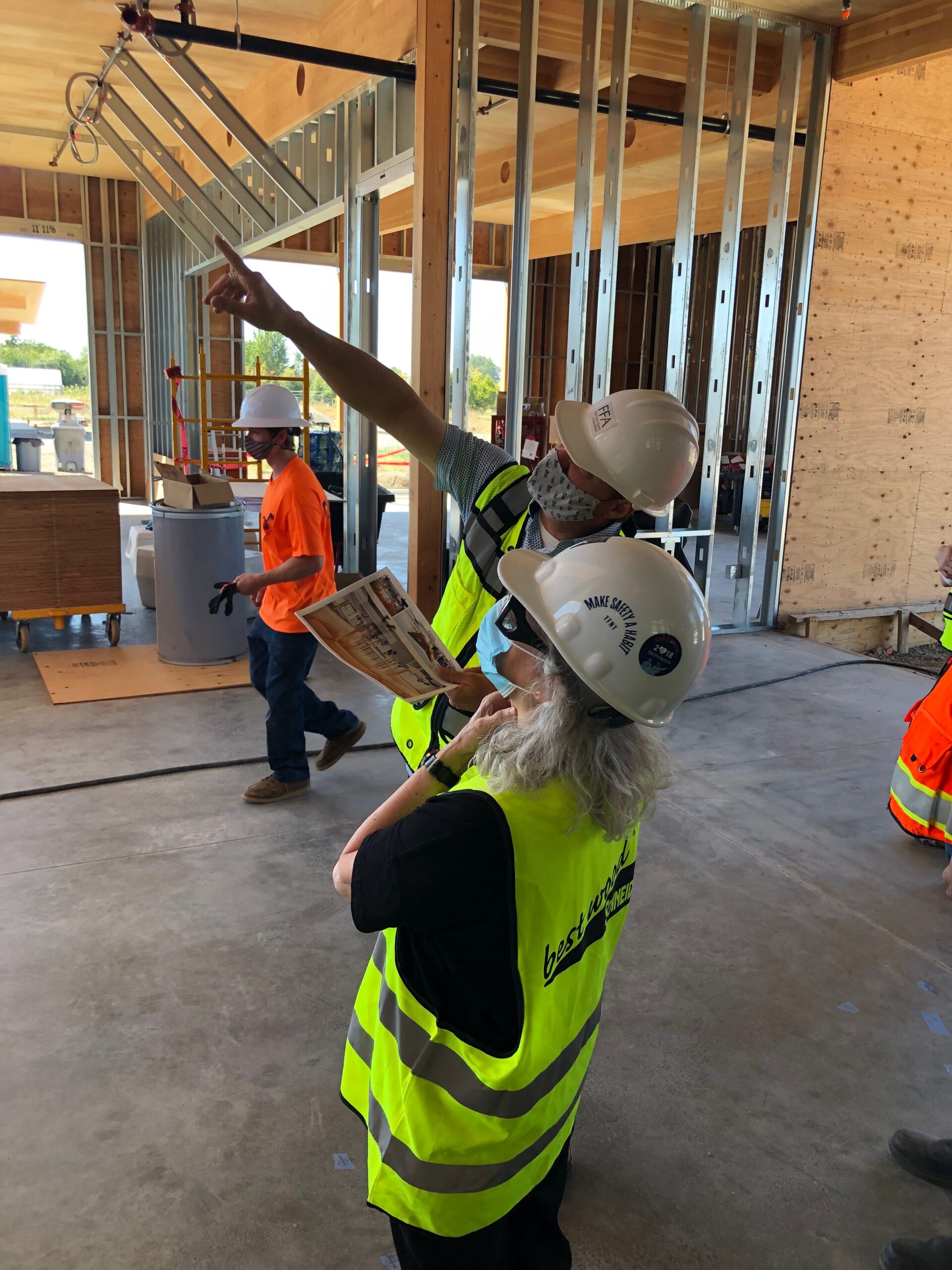 A man and a woman in yellow safety vests and hard-hats inside a building under construction
