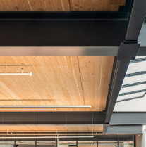 A detail photo showing a portion of a mass timber ceiling supported by a steel structure, next to a row of skylights