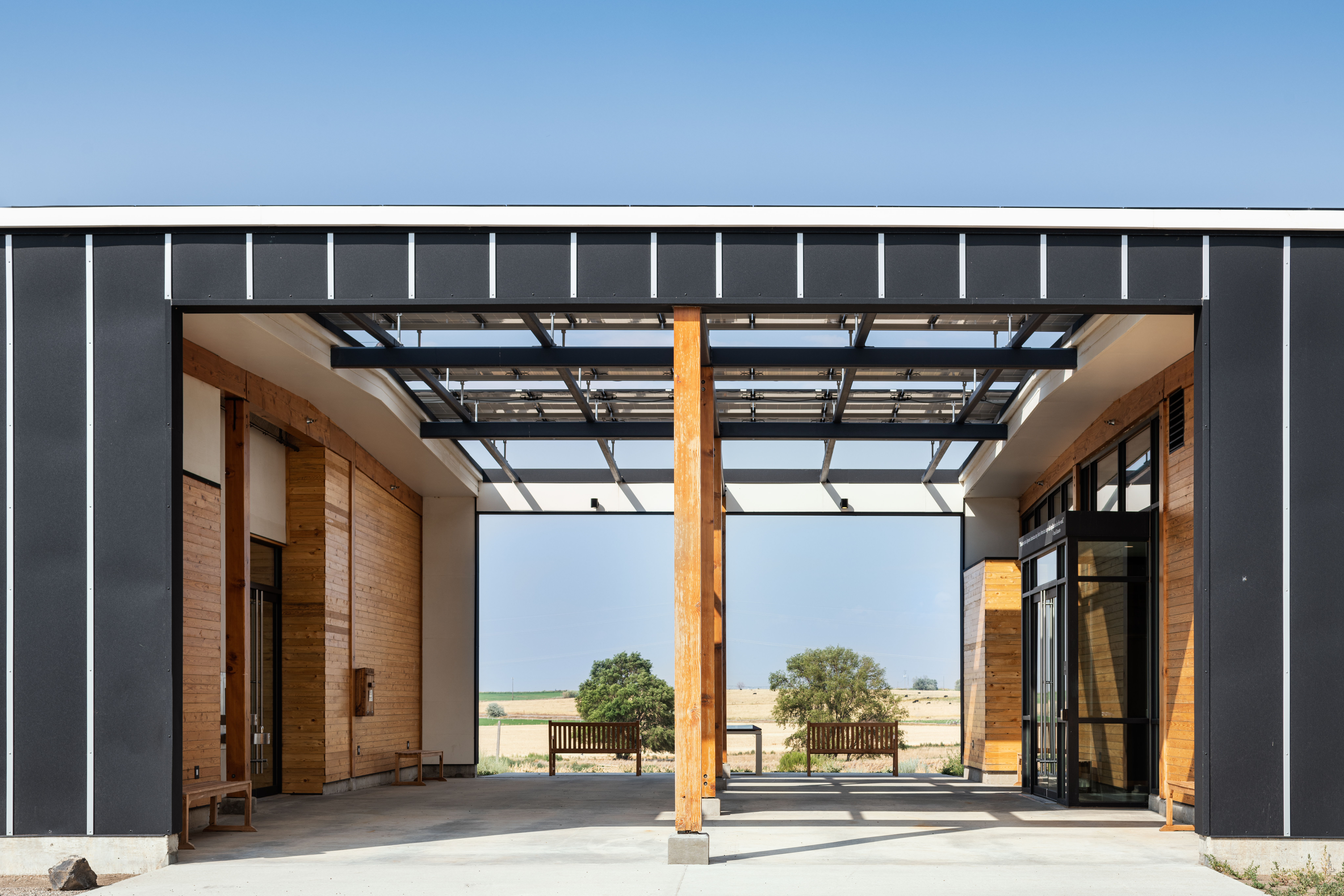 The breezeway of a one-story building looking through to a vast empty landscape, save for two trees in the distance