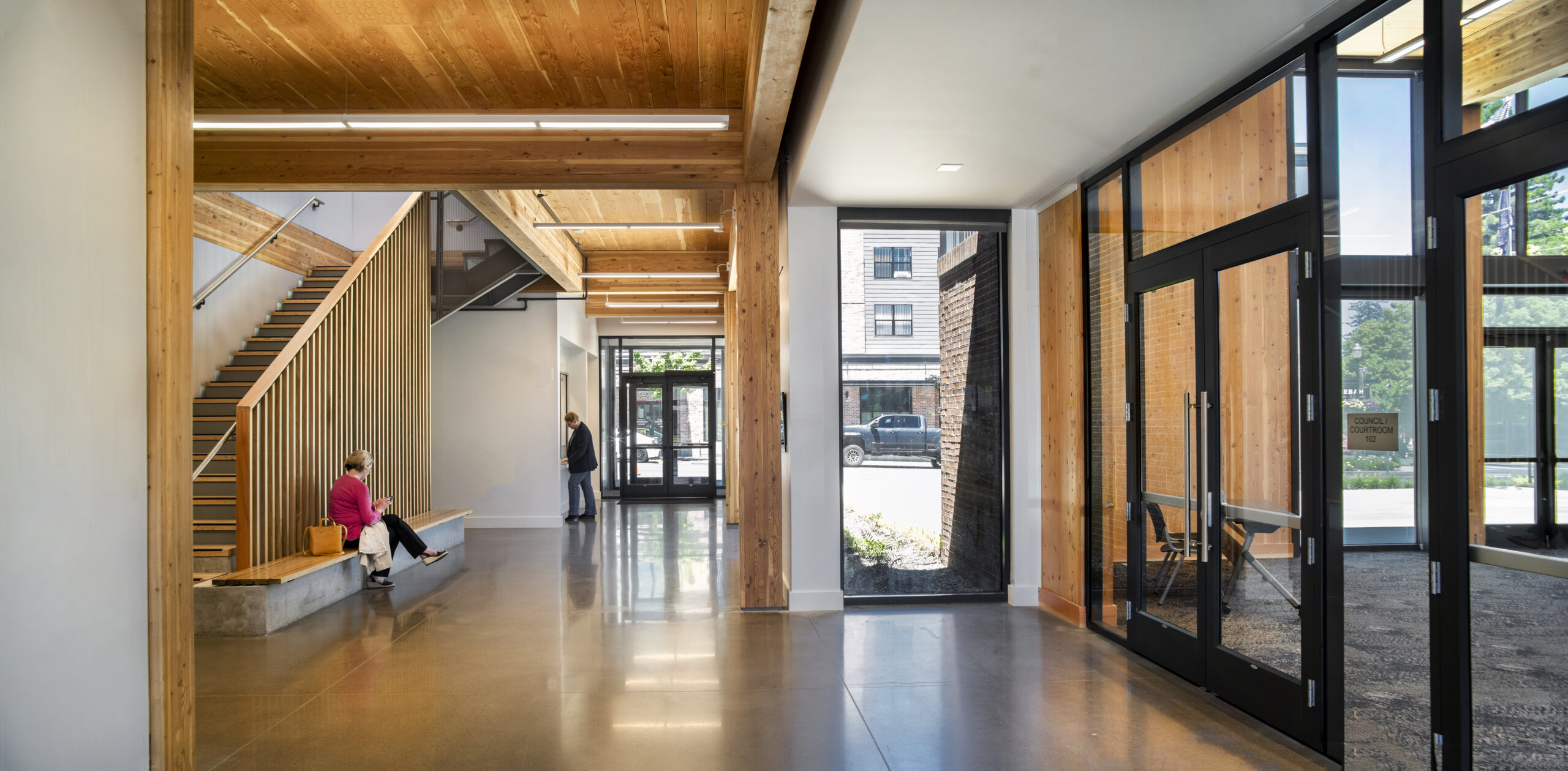The lobby of a city hall featuring mass timber ceilings and stairway and polished concrete floors.