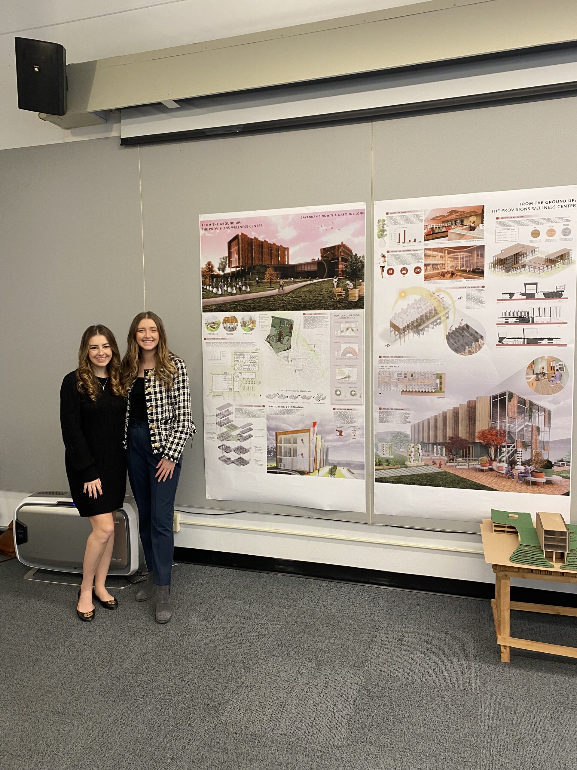 Tow young women standing in front of large print outs of their master of architecture presentations