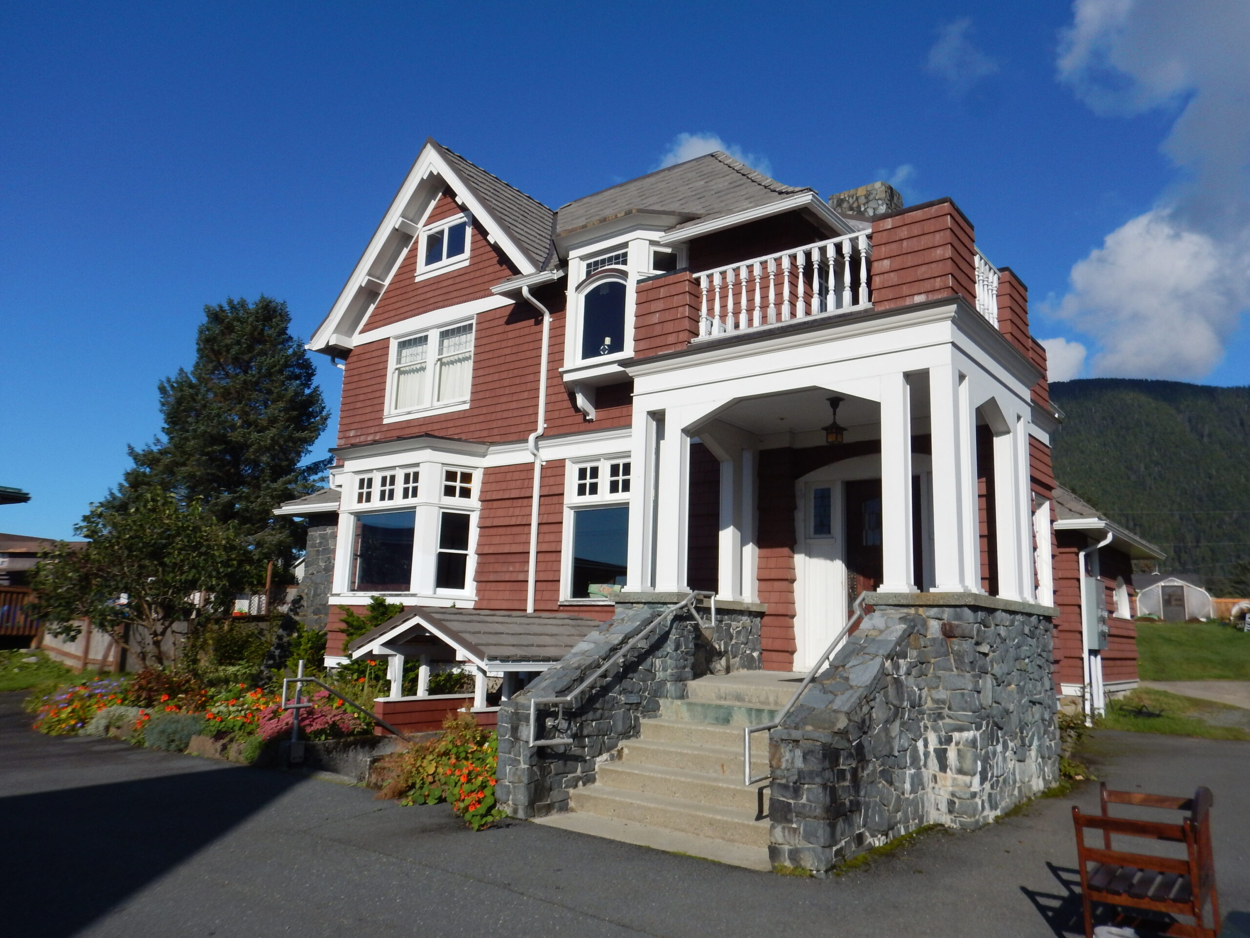 A historic, Victorian style house painted deep red with white trim. A stone and concrete staircase lead to the front entrance.