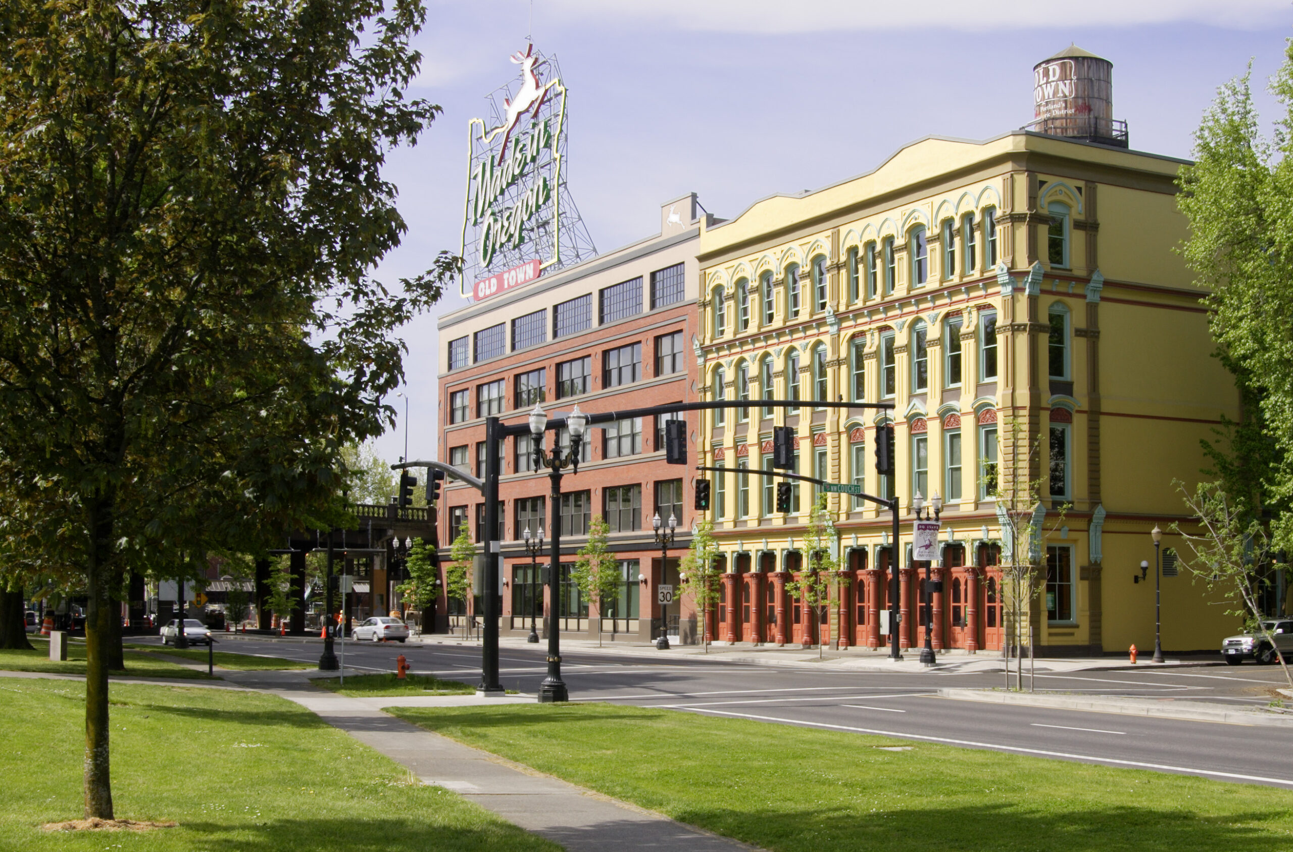 Two adjacent historical buildings, one painted in bright collors, and the other covered in brick with a large, neon White Stag sign on its roof.