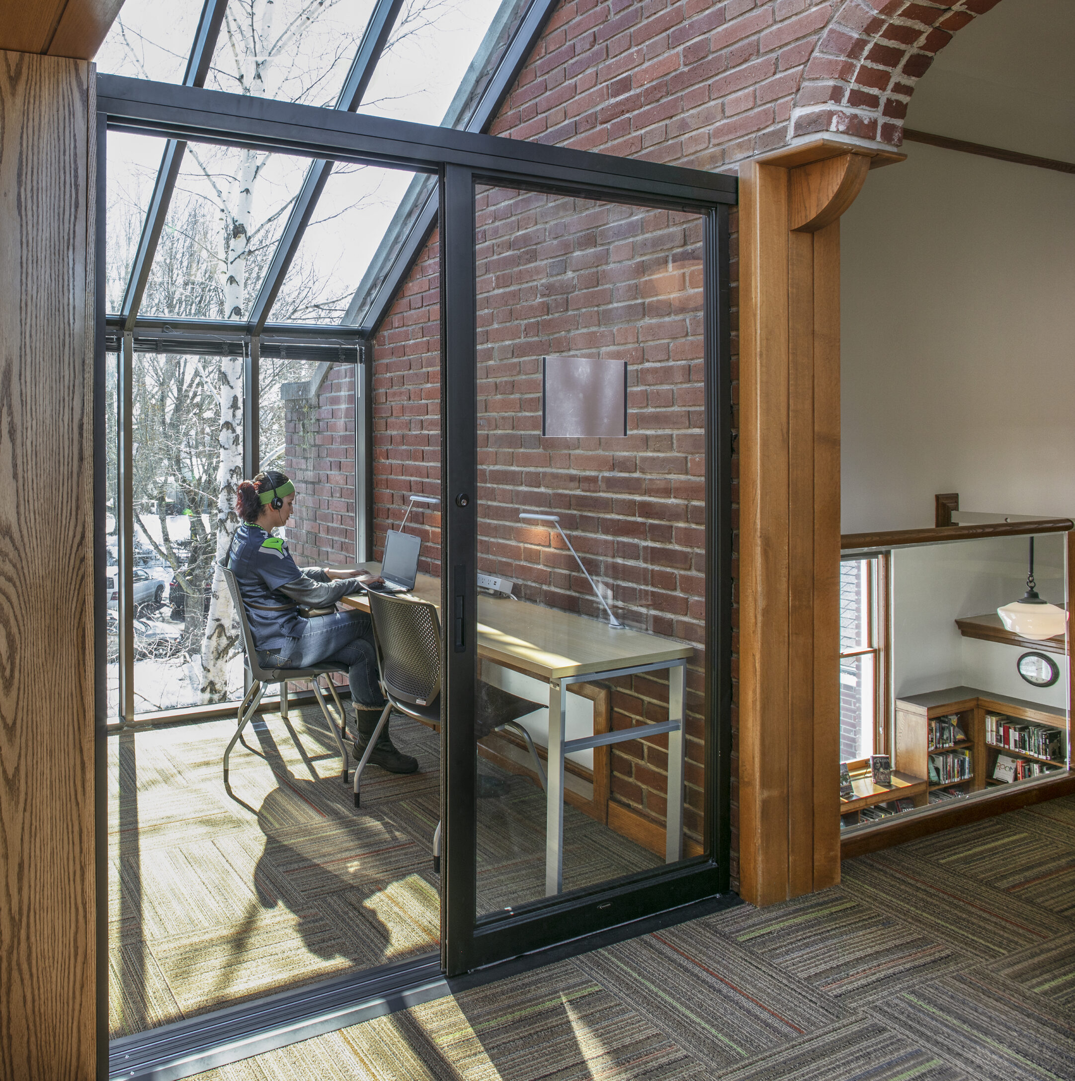 A teenage girl sits inside a glassed-in study nook, working on a computer