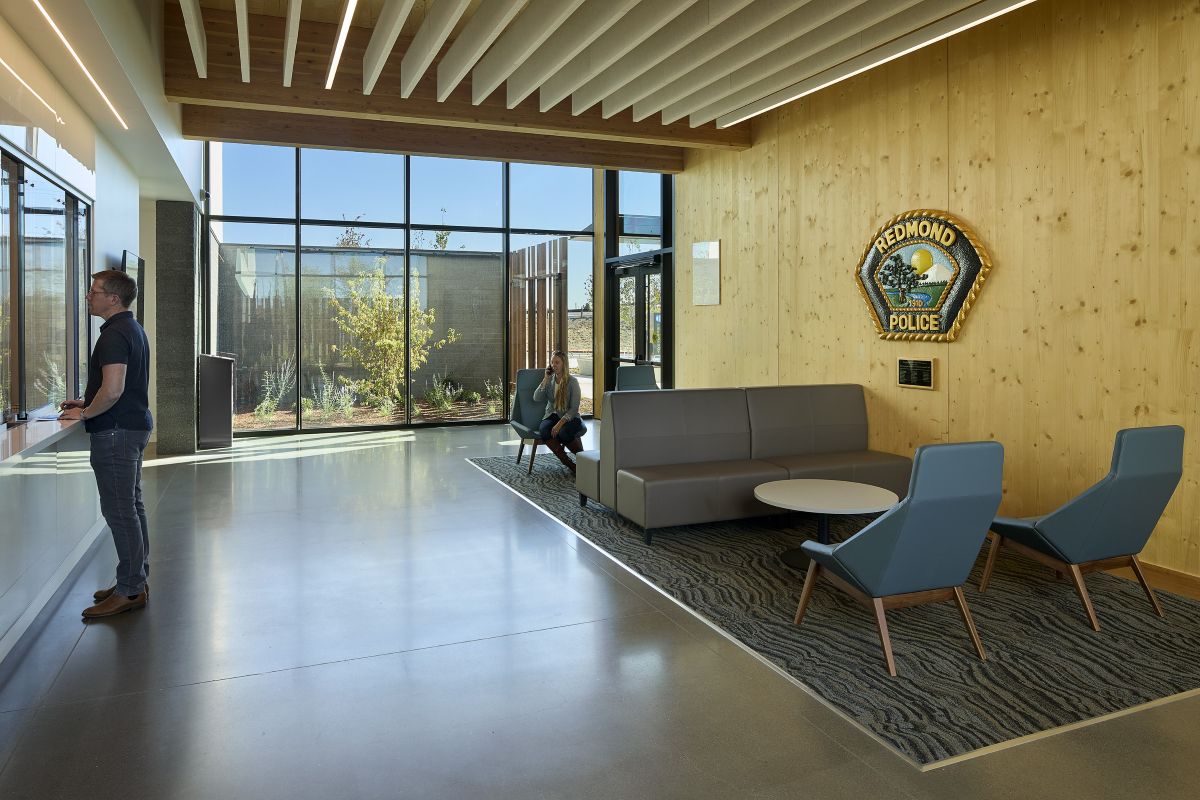 Visitors use the light-filled Redmond Public Safety Facility lobby, featuring exposed mass timber, comfortable seating, and views to a landscaped courtyard.