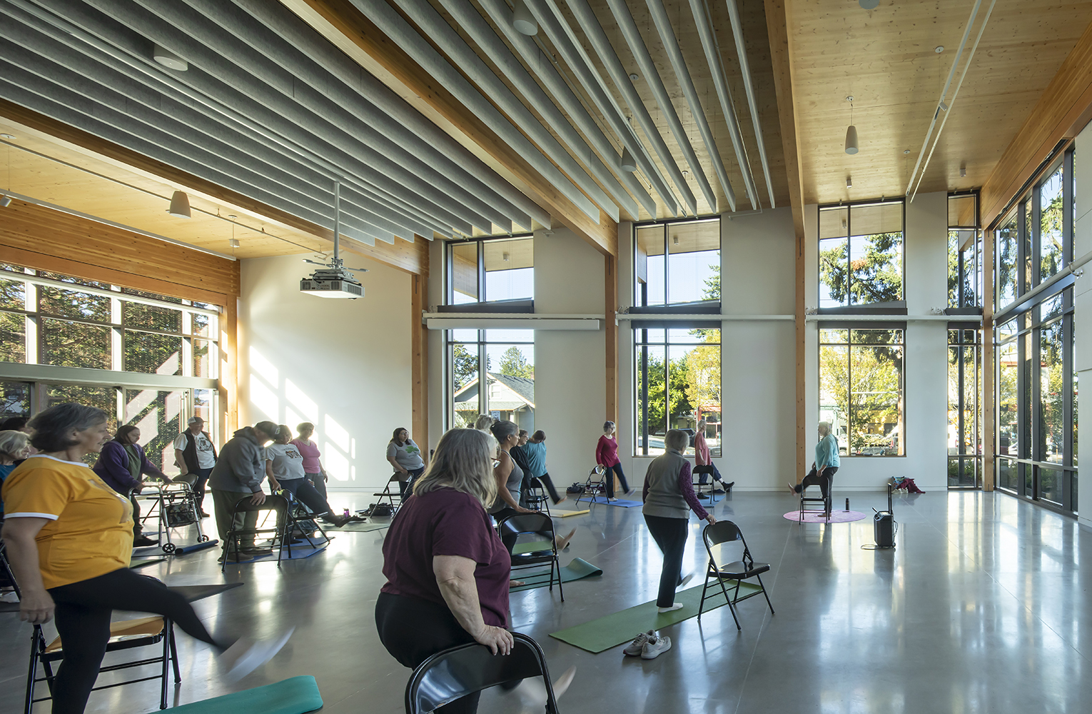 Community members participate in a chair yoga class inside the daylit event hall with exposed mass timber structure