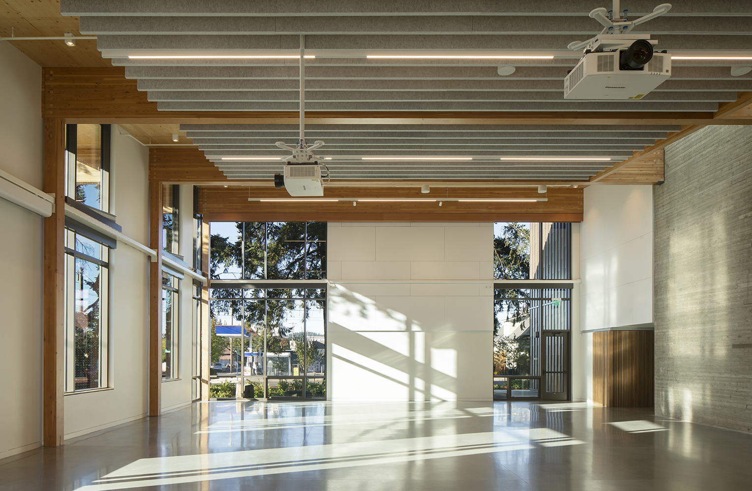 Sunlight fills the flexible event hall, highlighting exposed mass timber beams, acoustic panels, and tall windows