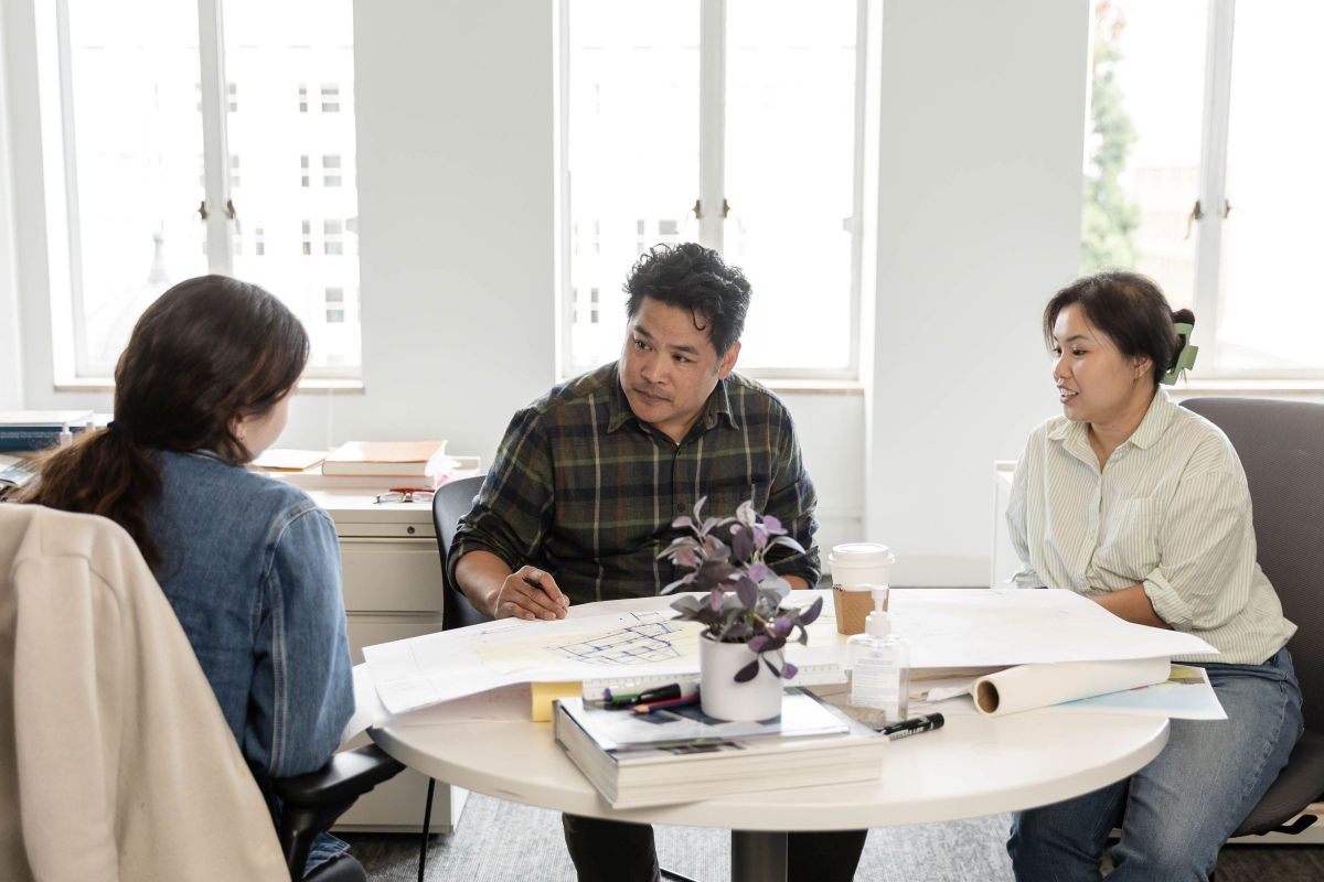 Three FFA architects collaborate around a table, reviewing drawings and discussing a project in the studio