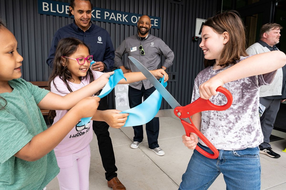 Children cut a blue ribbon at the Blue Lake Park Office opening while Metro staff and project partners celebrate.