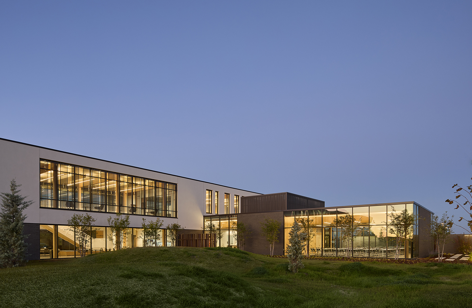 Evening view of the Redmond Public Safety Facility with illuminated interiors, large glass walls revealing exposed mass timber, and landscaped grounds surrounding the building
