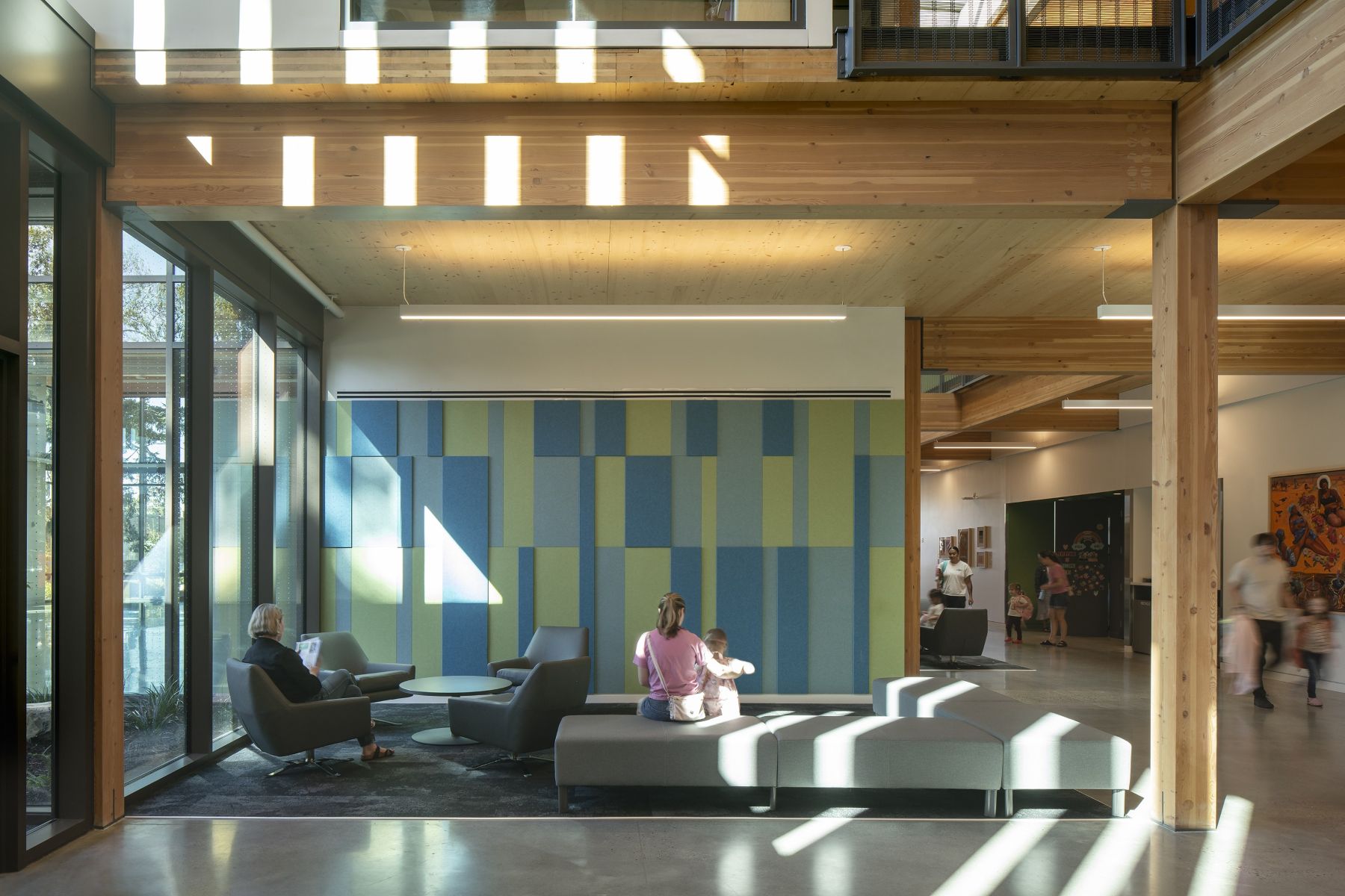 Visitors gather in the light-filled Mt. Scott Community Center lobby, framed by exposed mass timber and colorful panels.