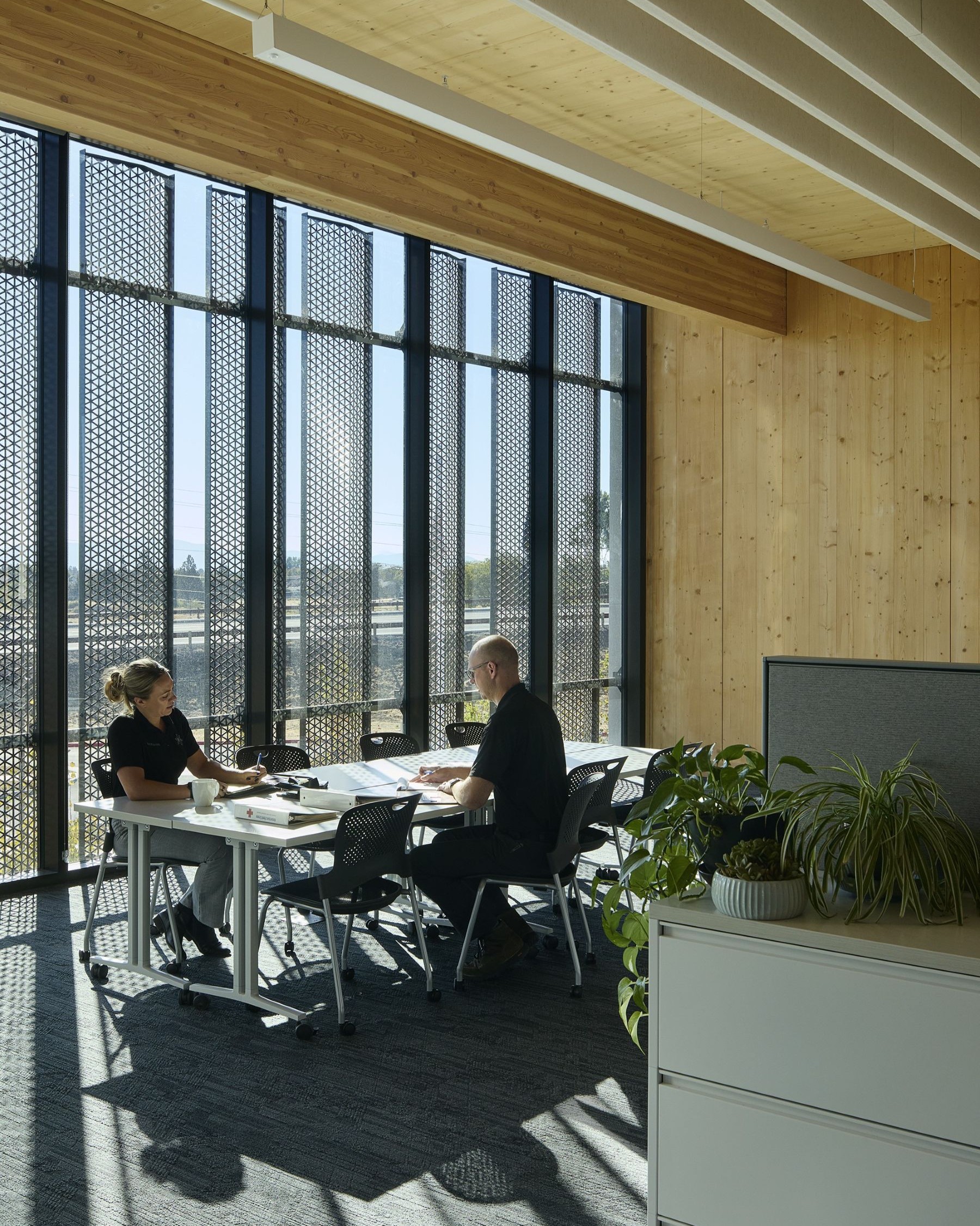 Two staff members collaborate at a table in the Redmond Public Safety Facility, surrounded by mass timber, filtered daylight, and acoustic ceiling panels.